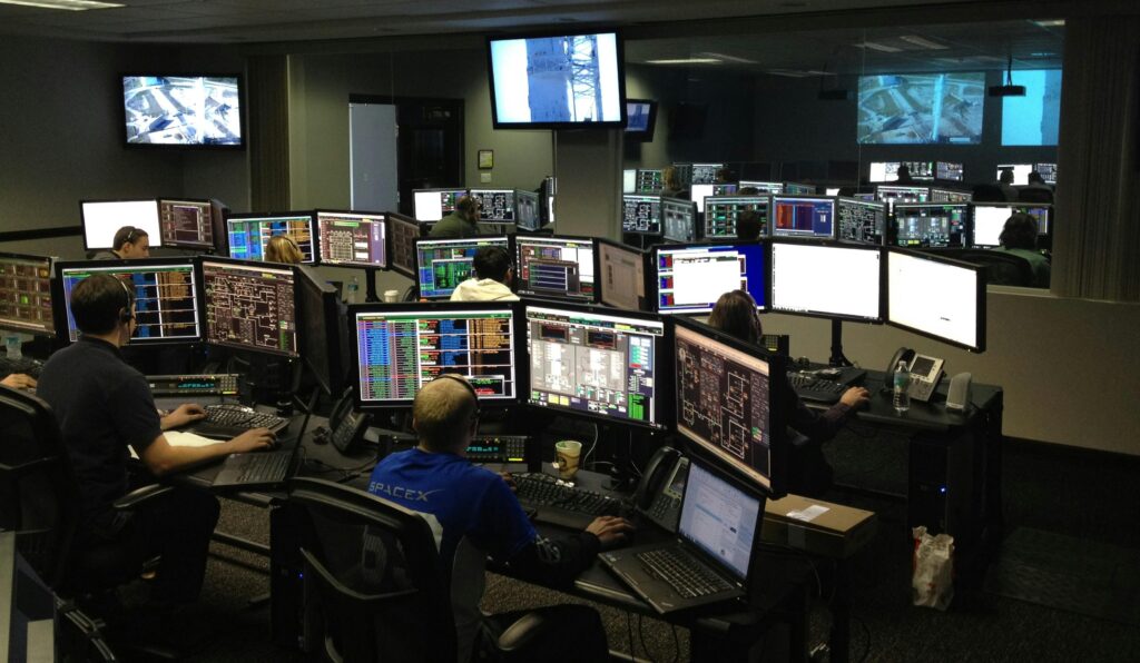 pexels-photo-256219-256219 A bustling control room with people working on multiple computer monitors.