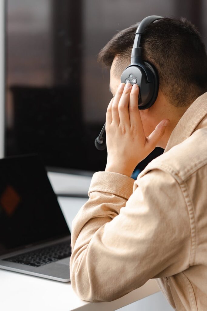 pexels-photo-7681302-7681302 A man wearing headphones works at a laptop in a modern office setting.